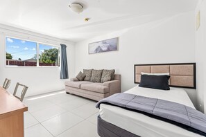 A bedroom with a bed, a sofa, a window, and a picture on the wall.