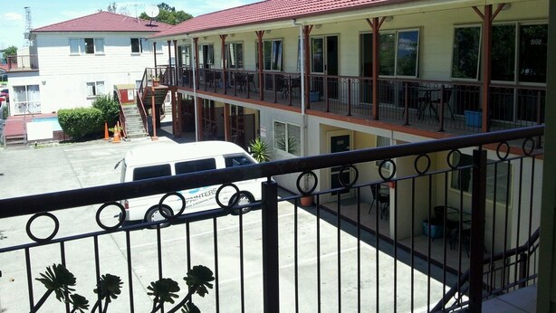 A two-story building with a red-tiled roof, balconies, and a parking area with a white van. - Avondale Motor Inn (Auckland)