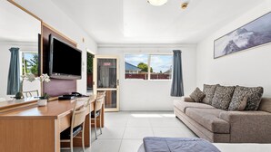 A modern living room with a sofa, a TV, a desk, and a large window. - Avondale Motor Inn (Auckland)