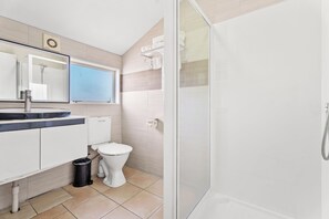 A modern bathroom with a glass shower enclosure, a white toilet, and a vanity with a mirror and towel rack.
