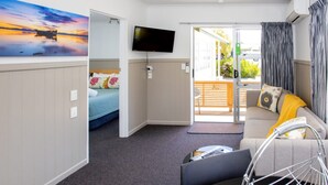 Habitación moderna y luminosa con cama, sofá y televisión. Se ve una puerta que da a un espacio exterior.
