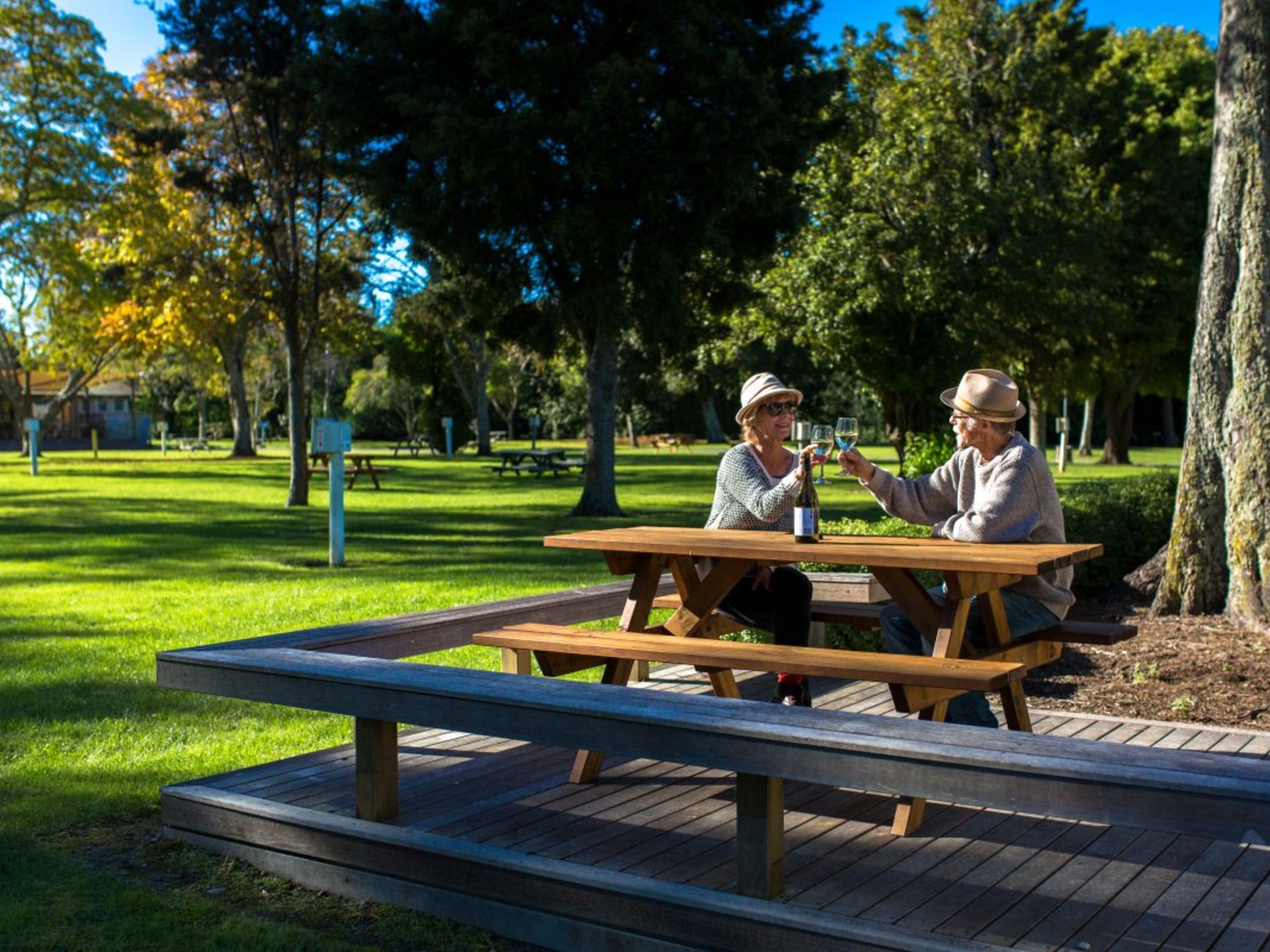 Una mesa de picnic en un parque, con bancos y árboles al fondo.