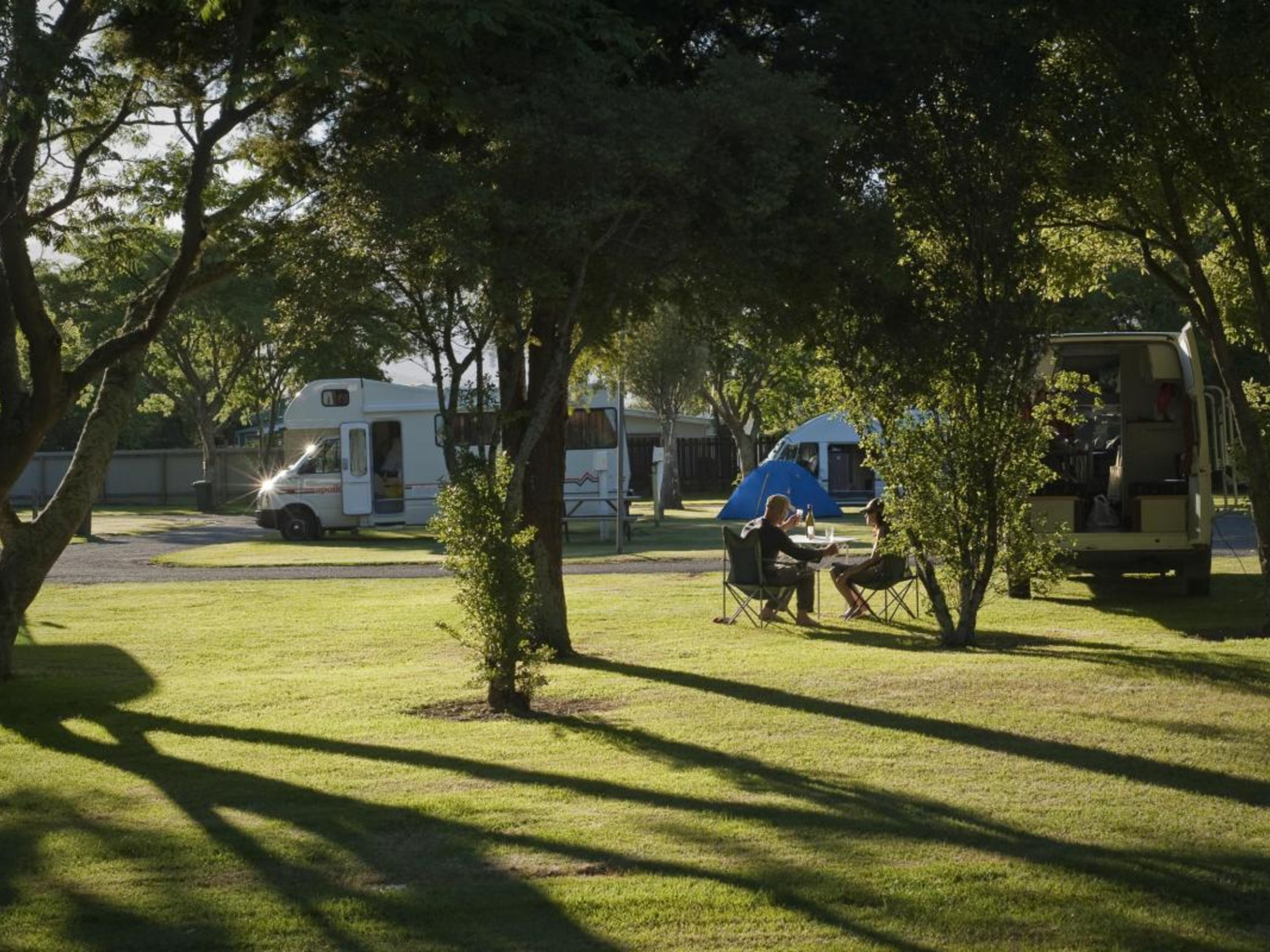 Een camping met campers en een tent, gazon en bomen.