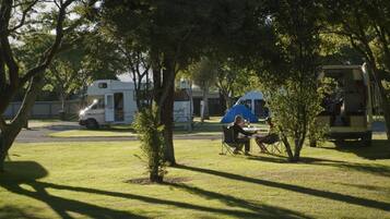 Een camping met campers en een tent, gazon en bomen.