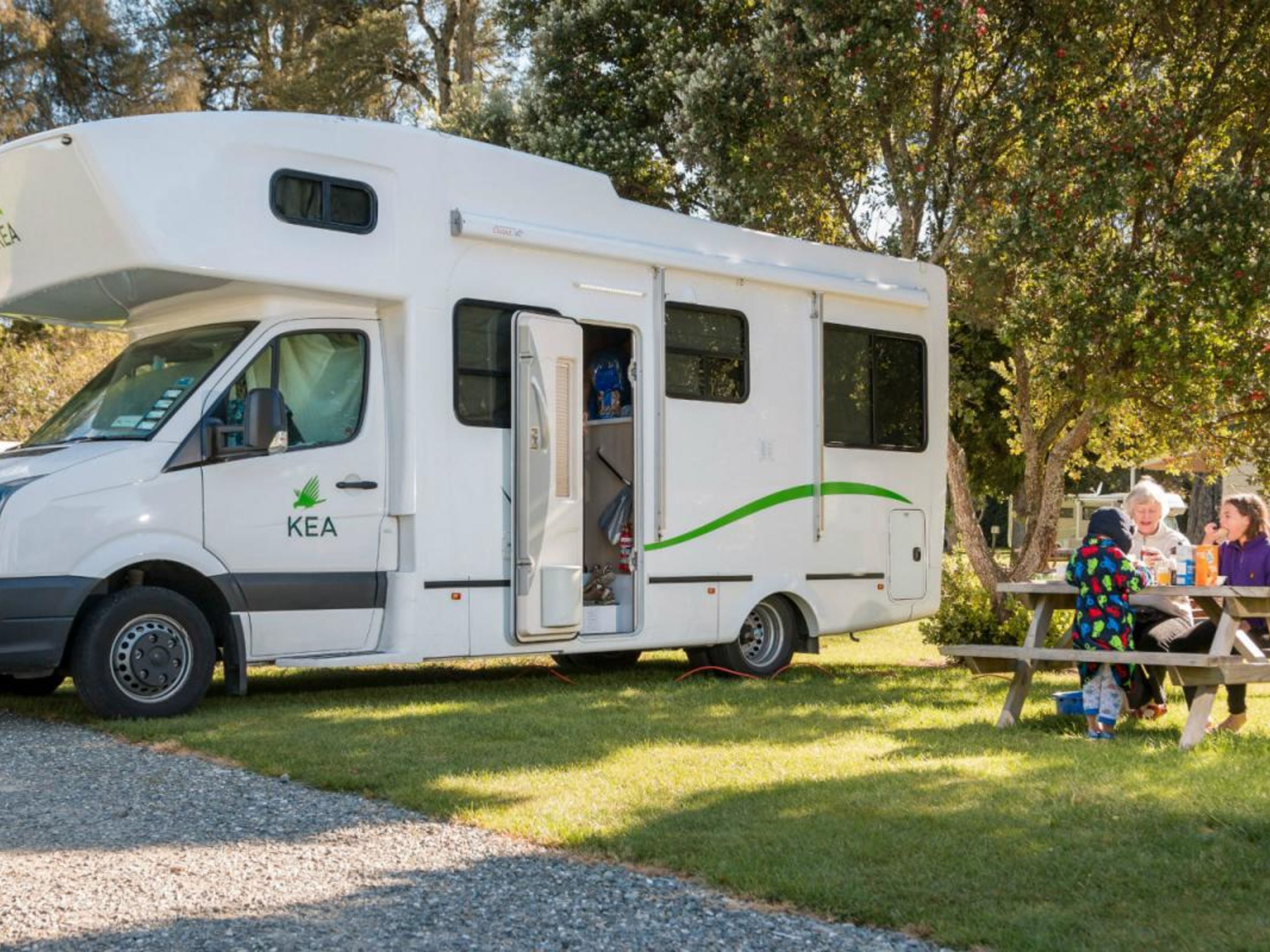 A white recreational vehicle with the logo "KEA" on the side, parked on a gravel path with grass on either side.