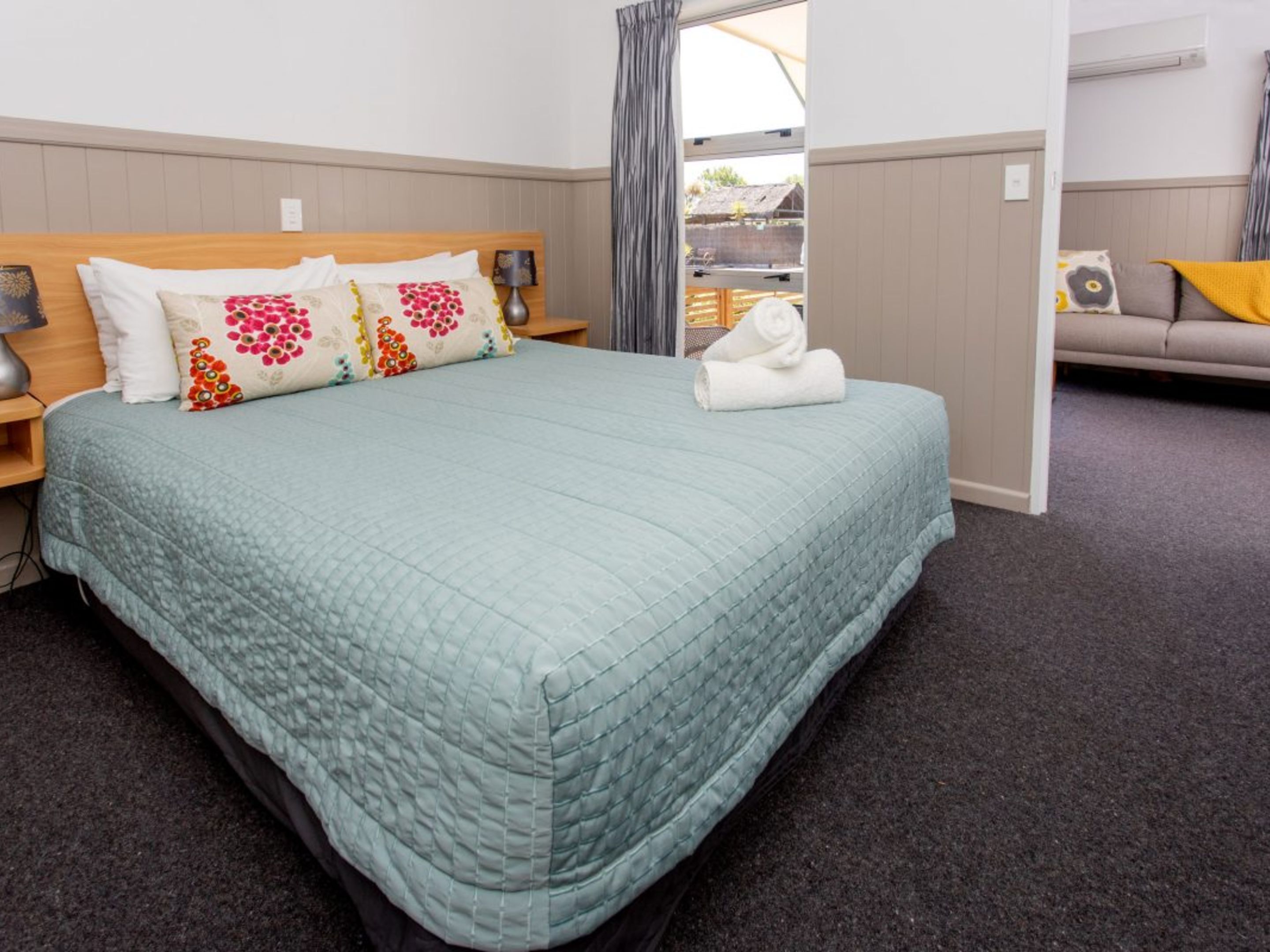 A neatly made bed with a light blue quilt, a wooden headboard, and decorative pillows.