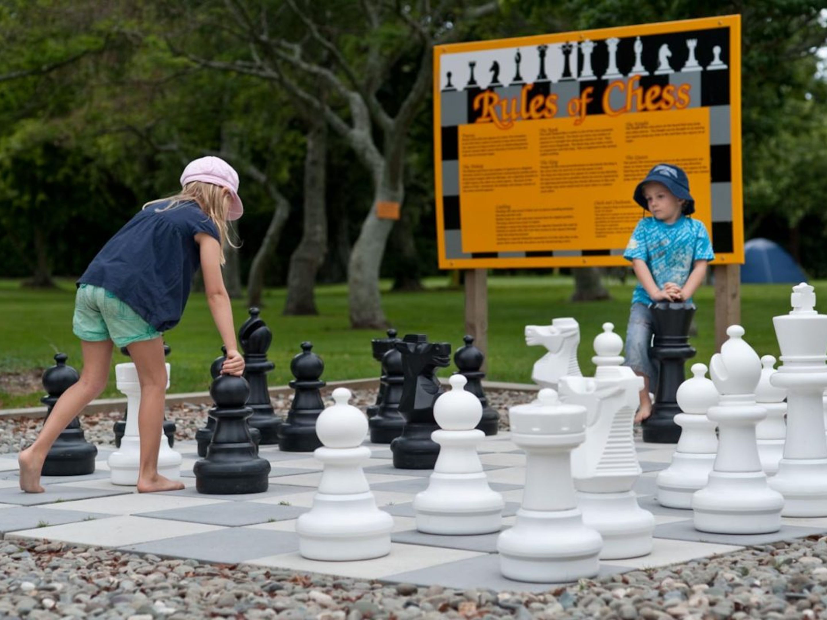 A chessboard with oversized pieces in a park setting.