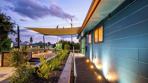 Un edificio moderno con fachada azul, terraza de madera y zona de estar exterior con plantas.