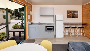 Una cocina compacta con microondas, pileta y refrigerador. Hay una zona de comedor con mesa y sillas, además de un banco en el exterior.