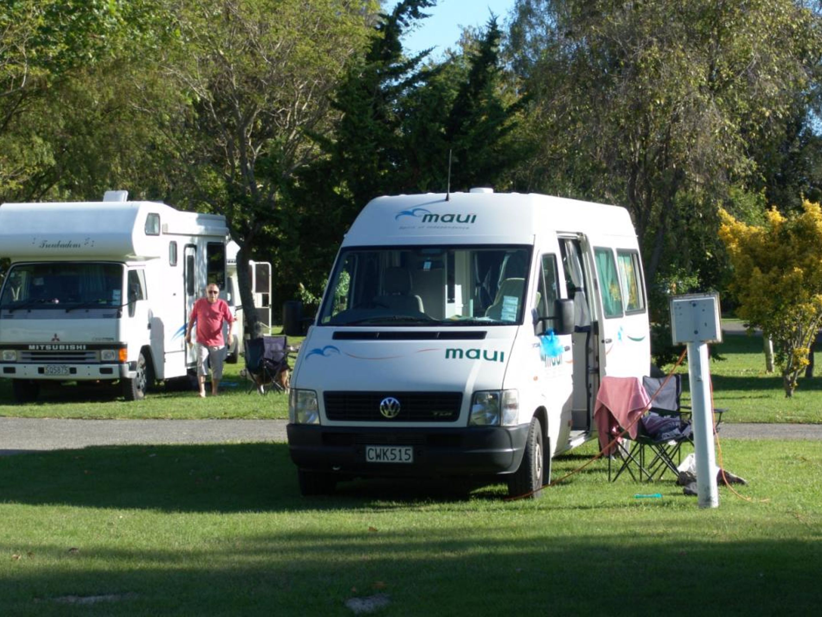 A white van with "maui" branding parked on grass, another van in the background, and a person walking.