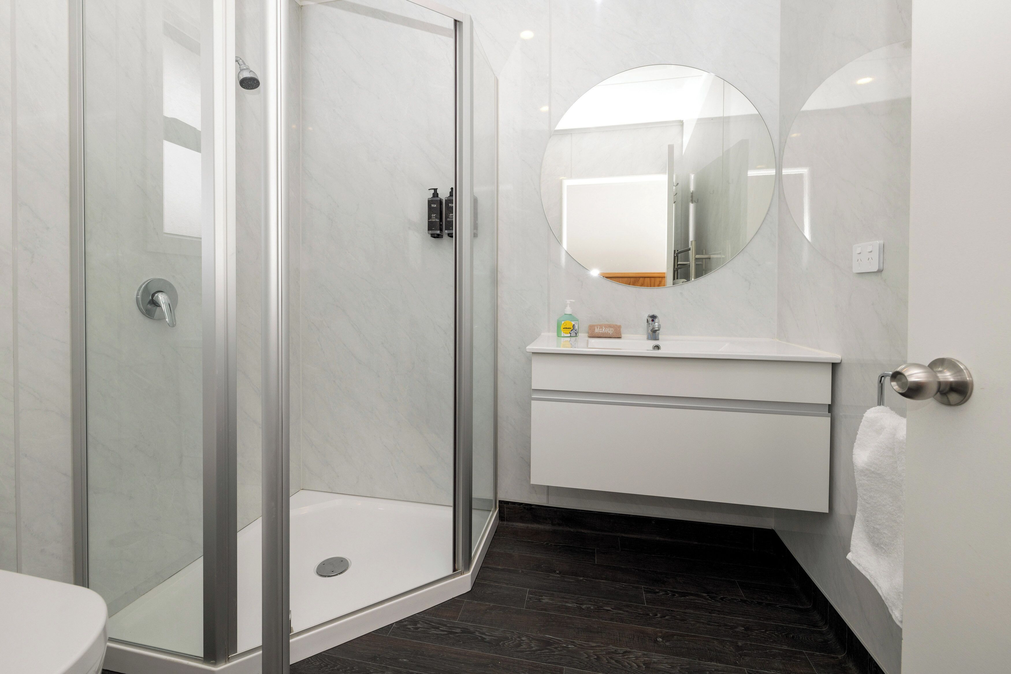 Une salle de bain moderne avec une douche à parois de verre, un lavabo blanc et un miroir rond.