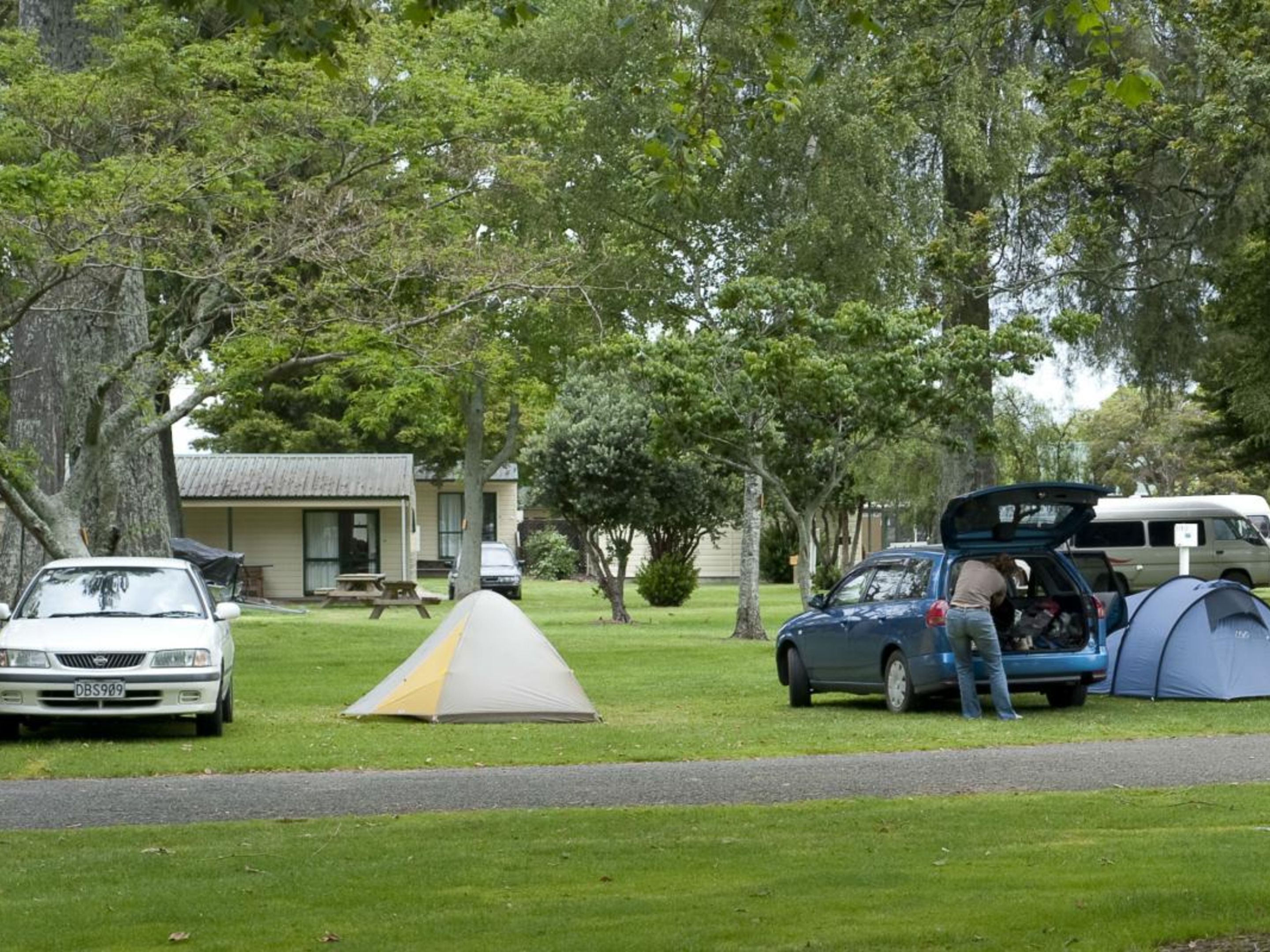 Un terrain de camping avec des tentes, une voiture et un bâtiment en arrière-plan.