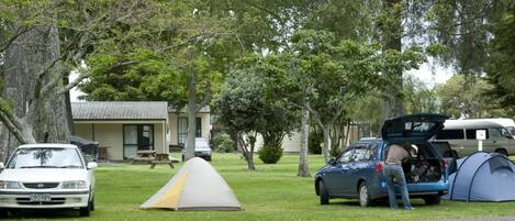 Un terrain de camping avec des tentes, une voiture et un bâtiment en arrière-plan.