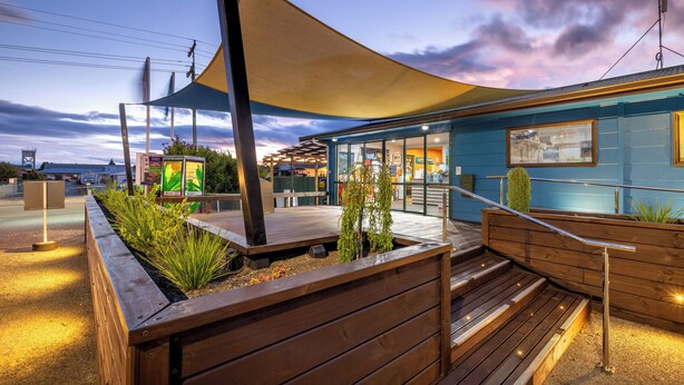 Un edificio moderno con terraza de madera, asientos al aire libre y un toldo grande.
