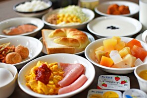 Un assortiment de plats pour le petit-déjeuner, notamment des œufs, du jambon, des croissants et des fruits.