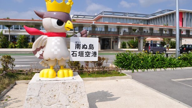 Eine große Vogelstatue mit Krone, ein Schild mit japanischem Text und ein modernes Gebäude im Hintergrund.