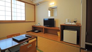 Ein Hotelzimmer mit Fernseher, kleinem Kühlschrank, Schreibtisch mit Laptop und Stuhl.