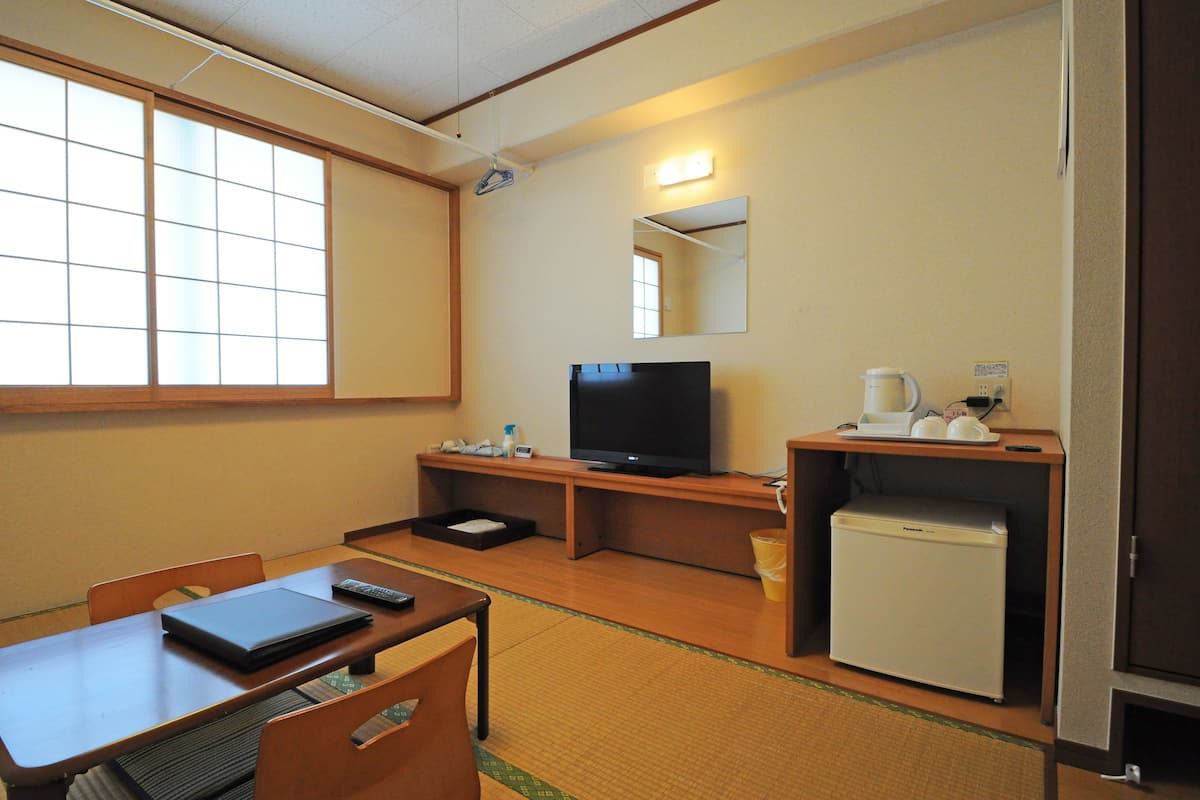 Hotelkamer met televisie, een kleine koelkast, een bureau met een laptop en een stoel.