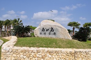 Ein großes Steinmonument mit Inschriften, umgeben von einer Steinmauer und Palmen.
