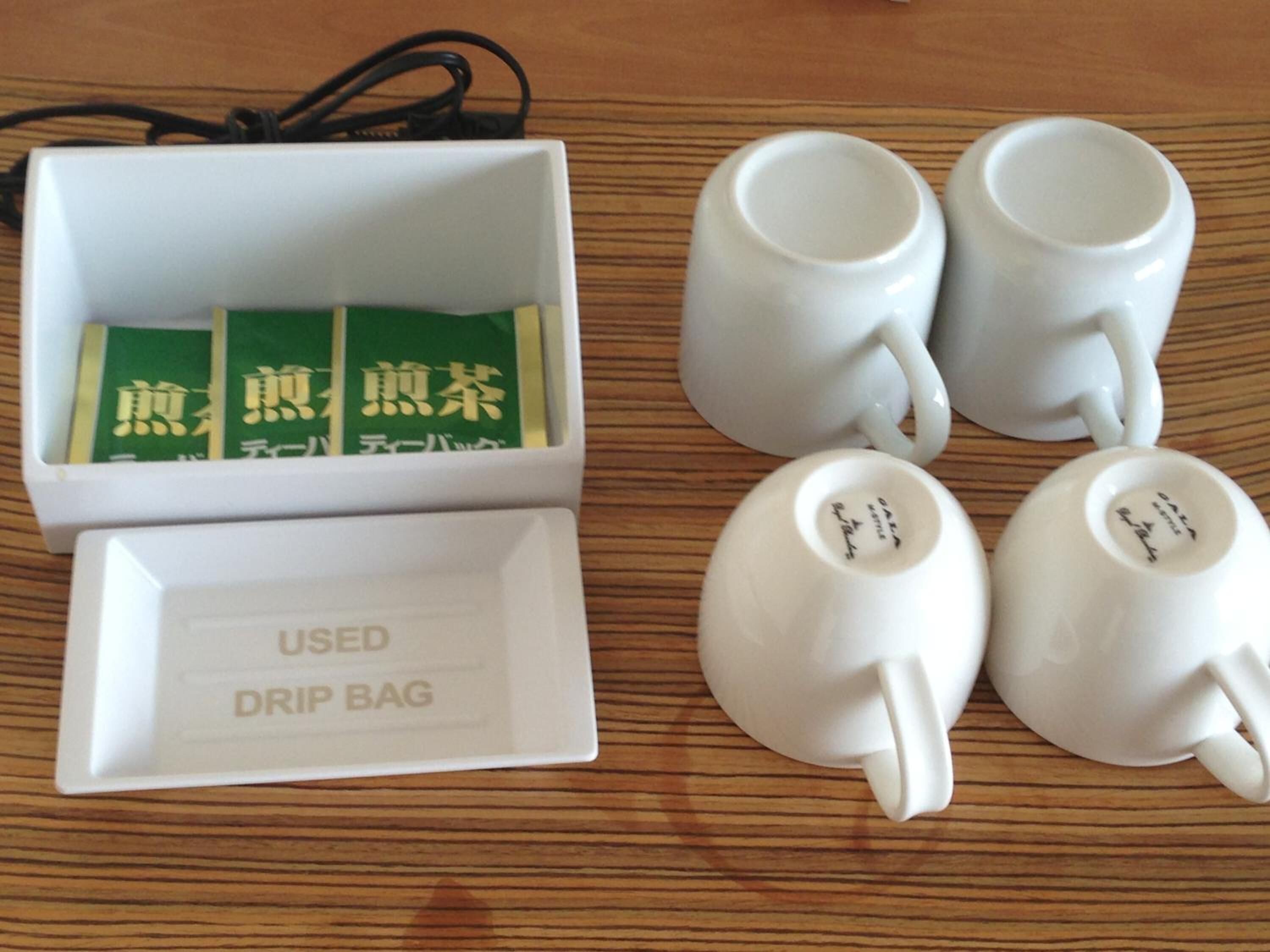 A white drip bag with used tea bags and two white teacups on a wooden surface.