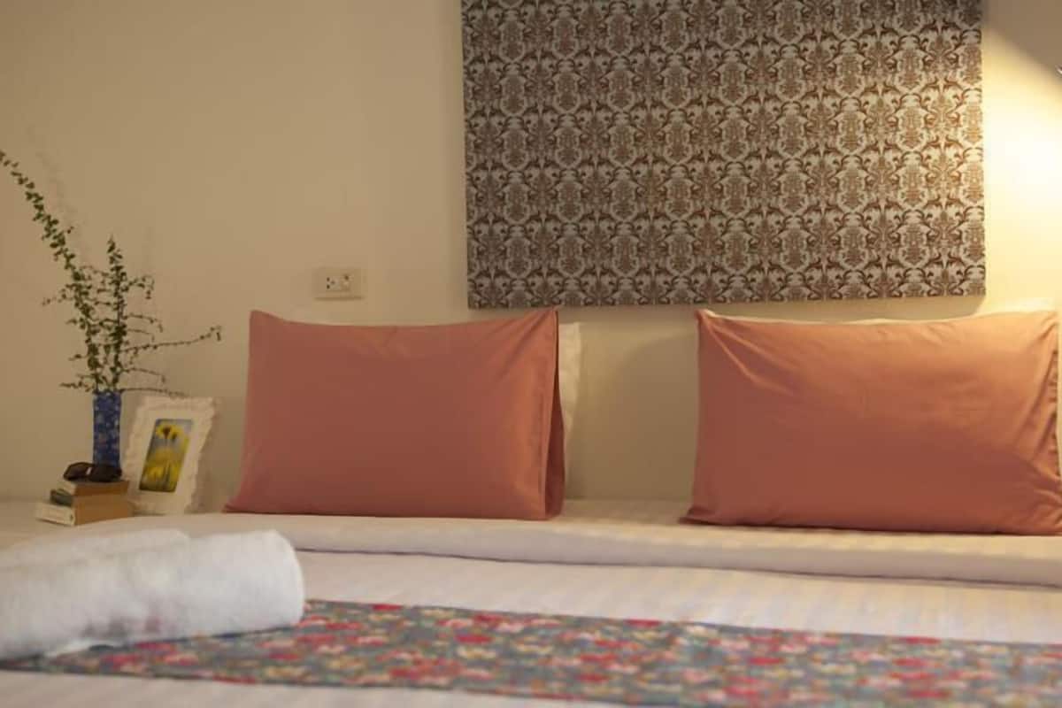 Un lit bien fait, recouvert d’une couvre-lit à motifs floraux, avec deux oreillers assortis, une lampe de chevet et un mur tapissé d’un papier peint à motifs.
