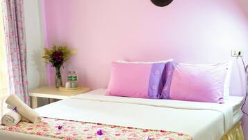 A neatly made bed with a floral bedspread, a bedside table with a vase of flowers, and a wall-mounted light fixture.