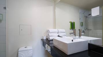Un baño moderno con un lavamanos blanco, un espejo y una zona de ducha.