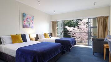 A hotel room with two beds, a balcony with a view of cherry blossoms, and a chair.