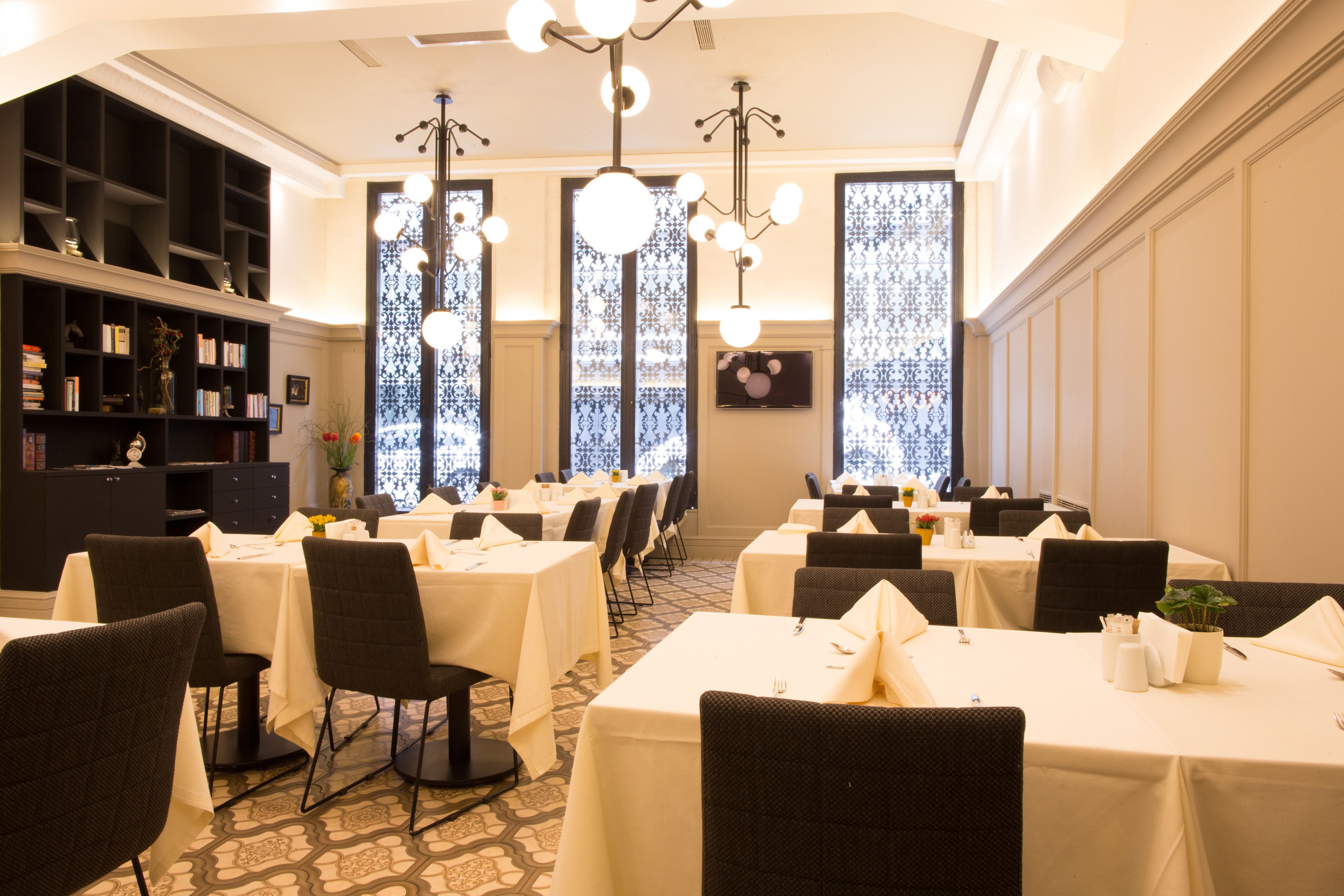 A dining area with multiple tables and chairs, a bookshelf, and decorative lighting.