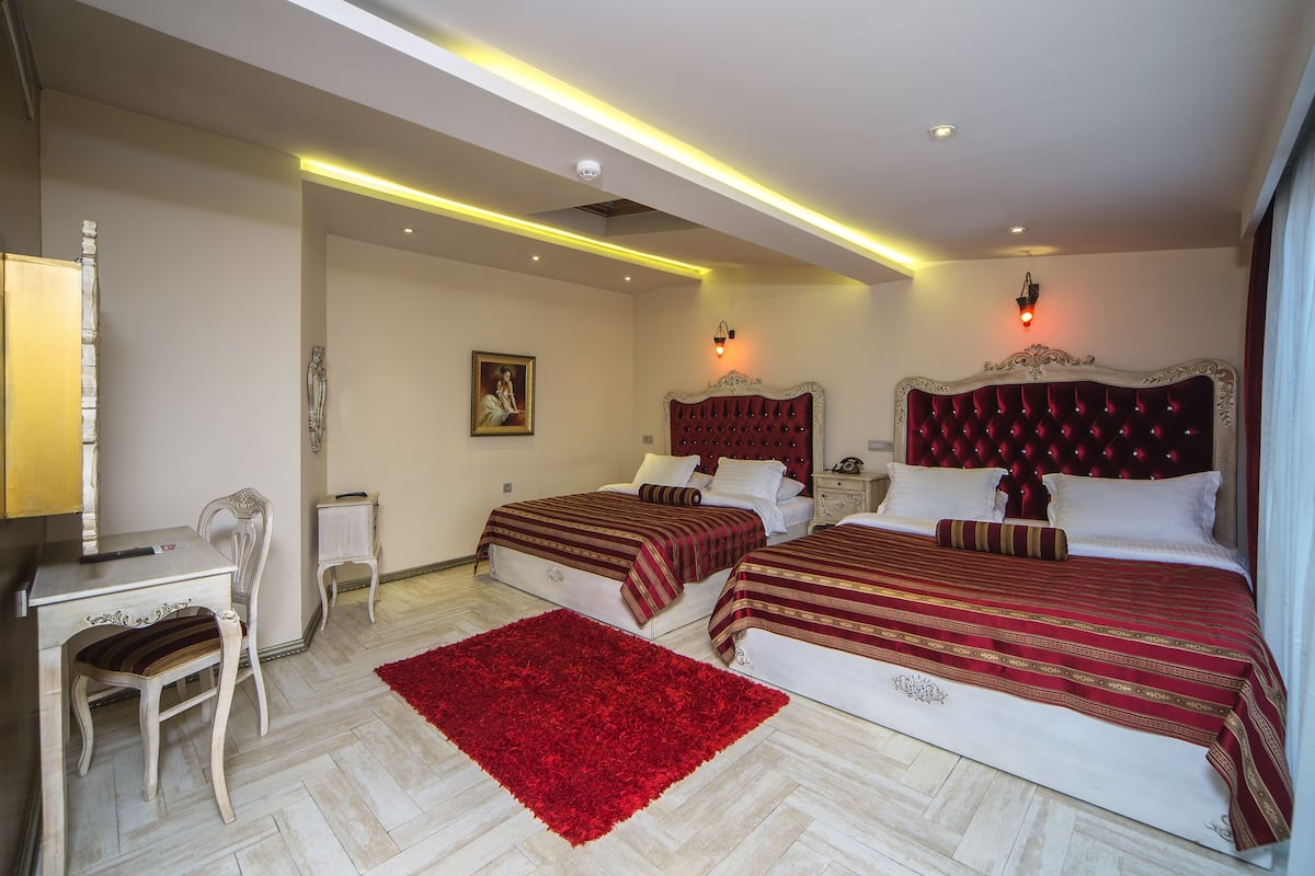 A hotel room with two beds, a desk, a chair, and a red rug.