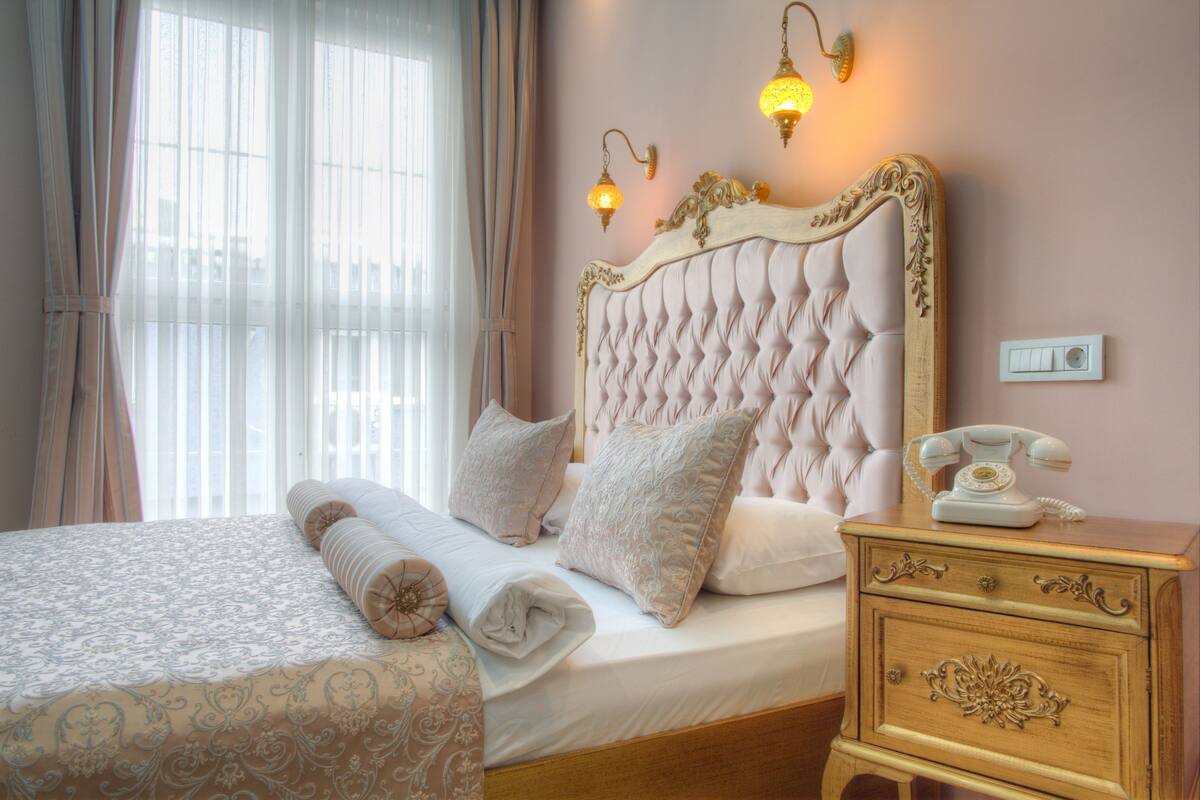 A neatly made bed with a patterned bedspread, a bedside table with a telephone, and two wall-mounted lamps.
