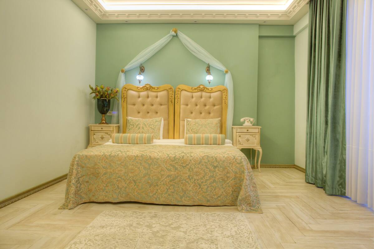 Ein Schlafzimmer mit einem großen Bett, zwei Nachttischen, einer Vase mit Blumen und einem grünen Vorhang.
