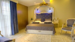A large bed with a tufted headboard, two bedside tables, a chair, and a large window with curtains. - Elegance Residence (Istanbul)