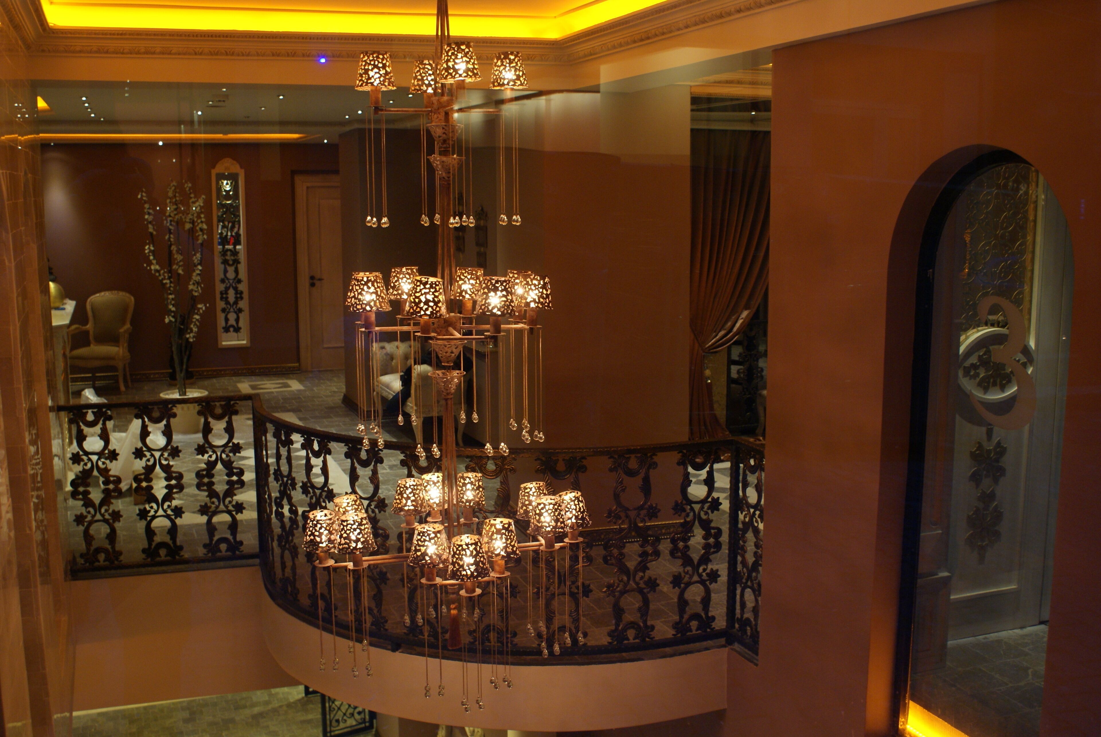 A grand chandelier with multiple light fixtures hanging from a curved railing in a luxurious interior space.