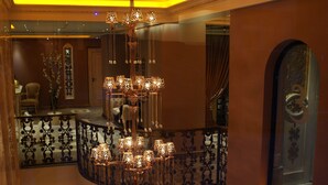 A grand chandelier with multiple light fixtures hanging from a curved railing in a luxurious interior space. - Elegance Residence (Istanbul)
