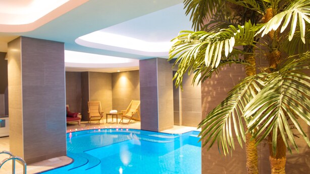 An indoor swimming pool with a clear view of the pool area, lounge chairs, and palm trees. - Elegance Residence (Istanbul)