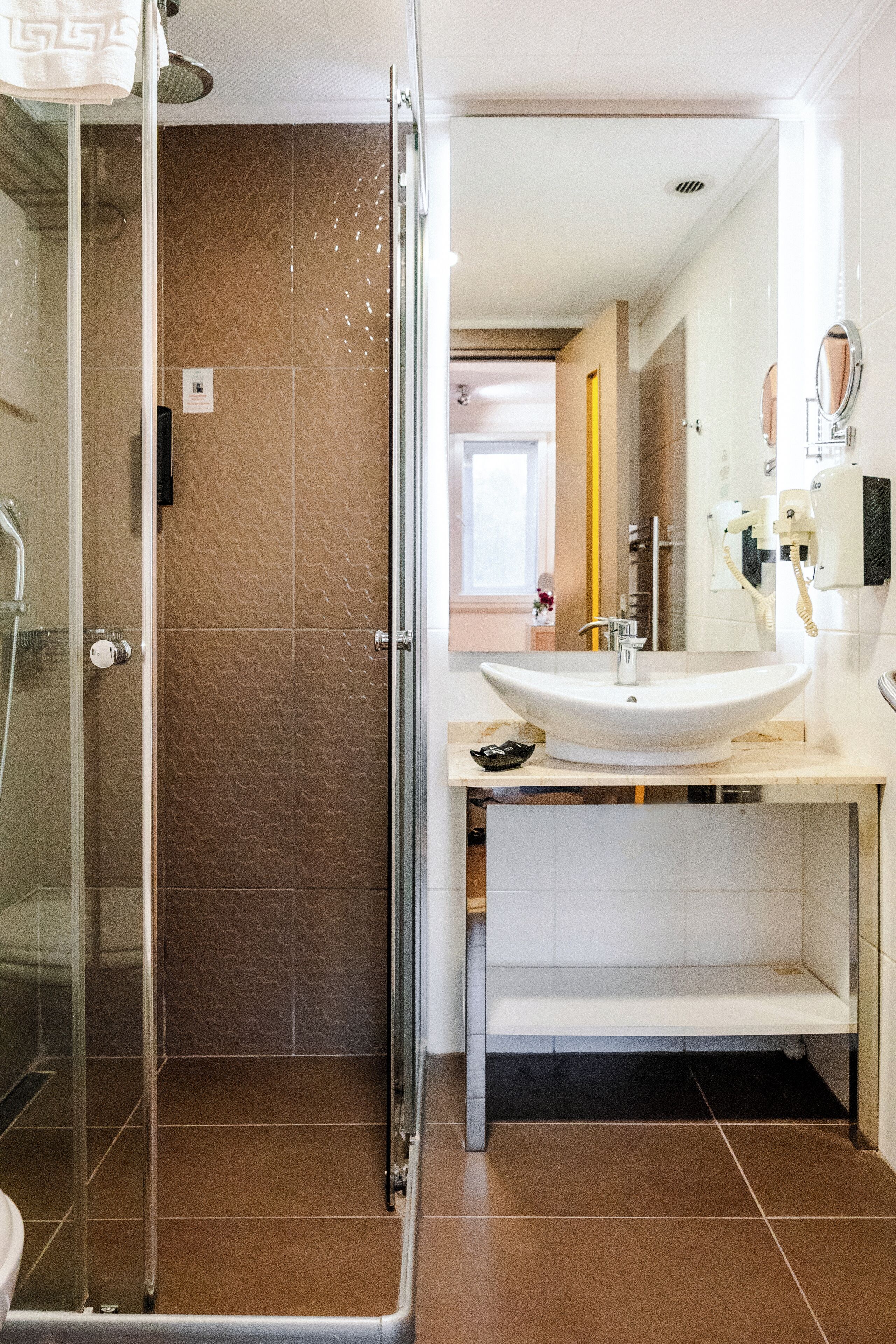 A bathroom with a glass shower enclosure, a white sink, and a mirror.
