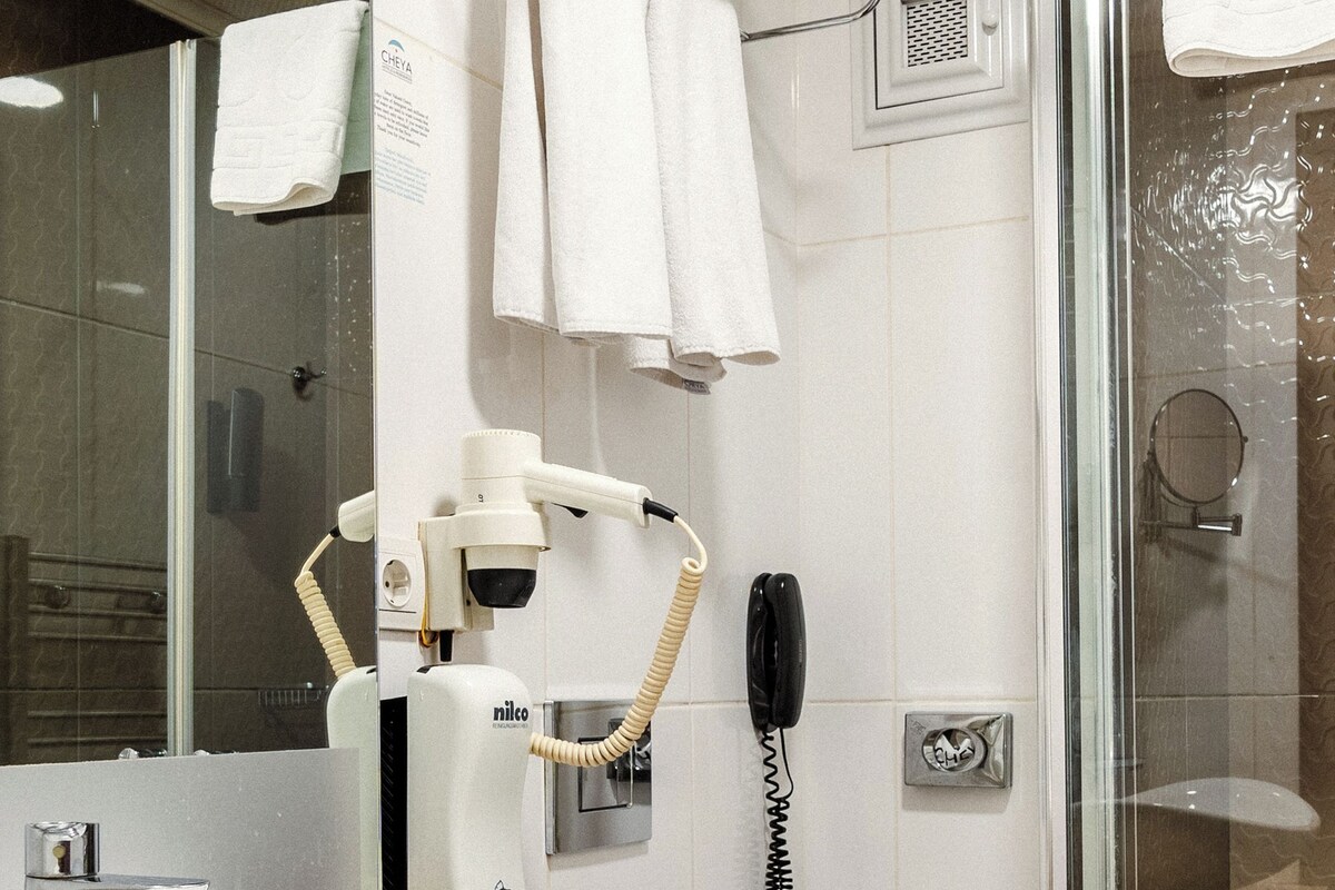 A bathroom with a sink, toilet, and shower. There is a towel rack with towels, a hairdryer, and a telephone.