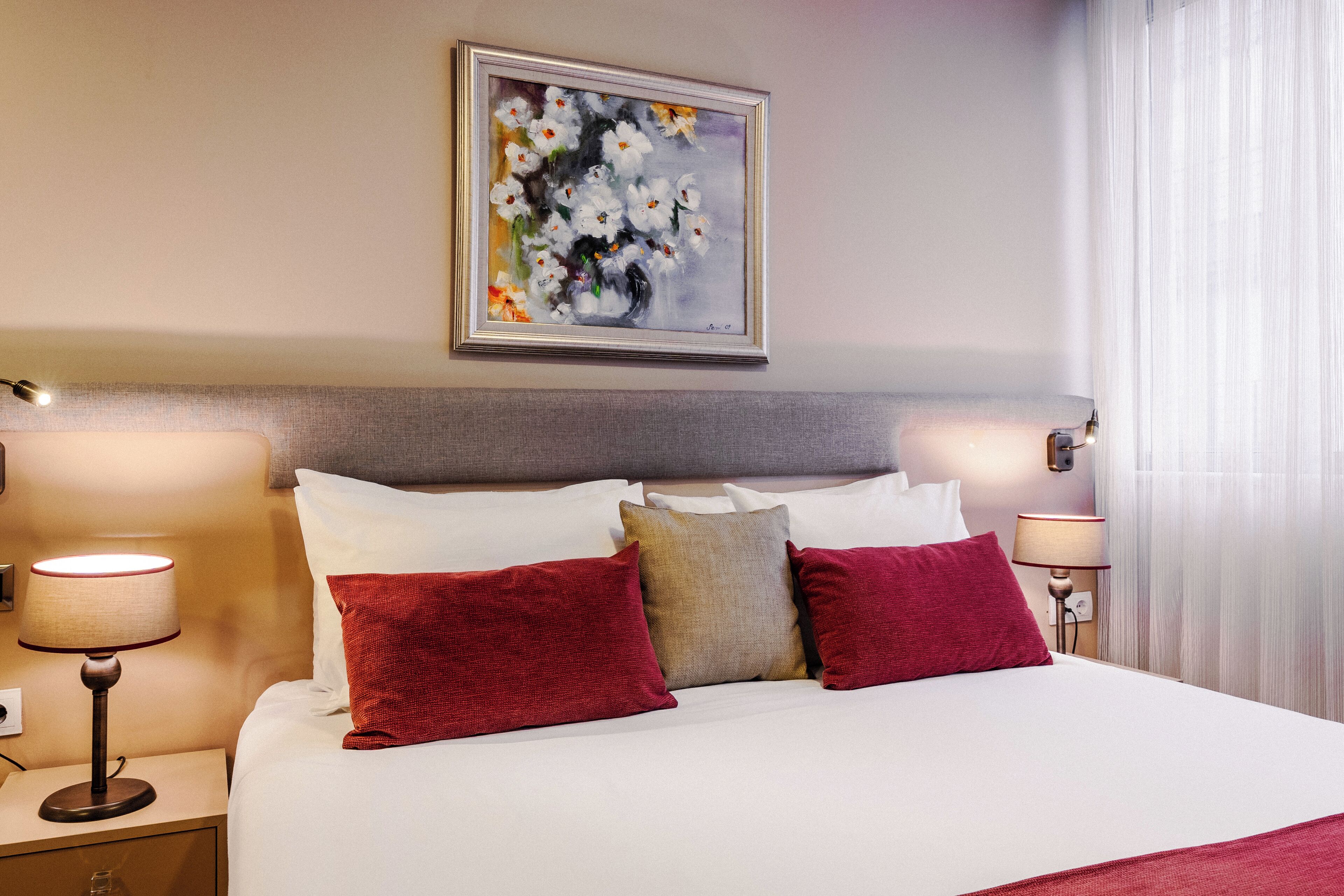Una habitación de hotel con una cama bien hecha, dos lámparas de noche y un cuadro en la pared.