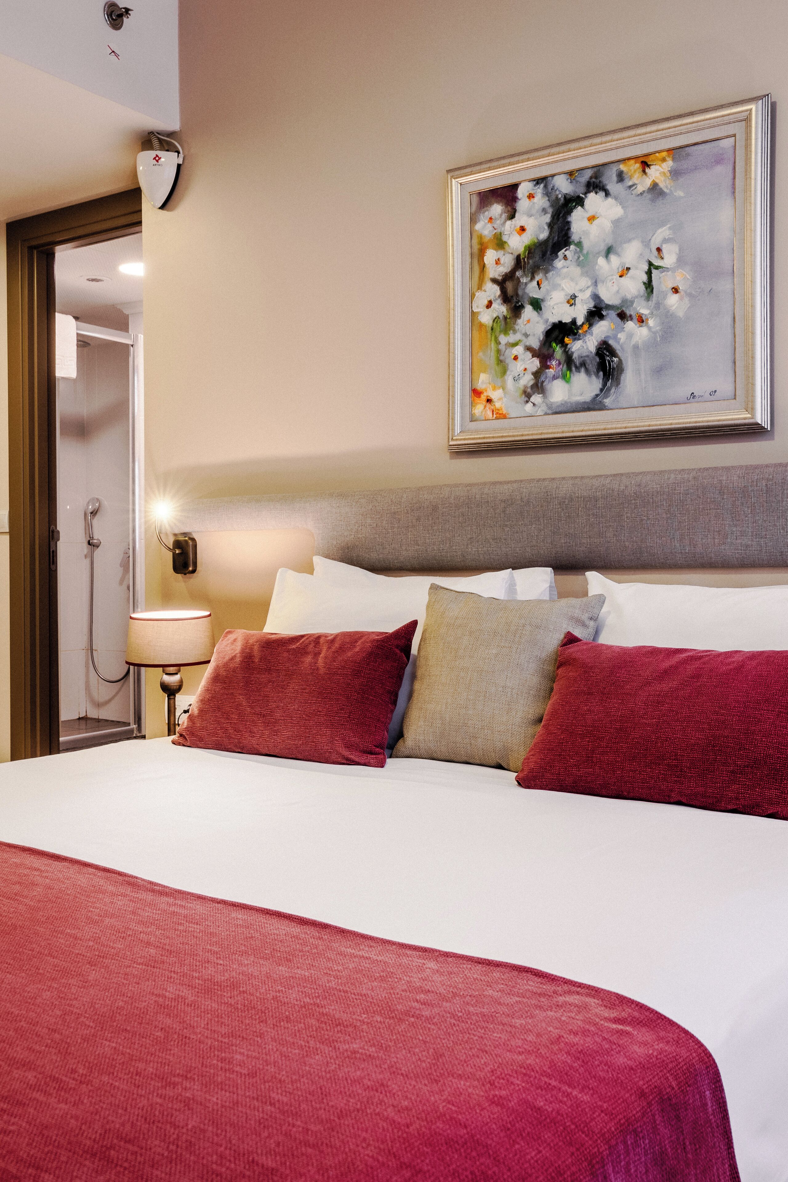 Une chambre d’hôtel avec un lit, des oreillers, un tableau, une lampe et un espace douche.