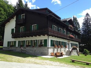 A two-story building with a balcony, stone foundation, and green shutters. - Casa Alpina Don Guanella (Macugnaga)