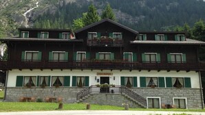 A two-story building with a stone facade, green shutters, and a balcony. - Casa Alpina Don Guanella (Macugnaga)