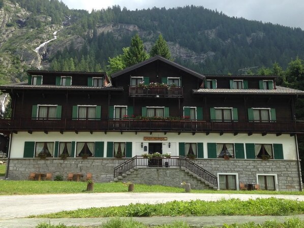 A two-story building with a stone facade, green shutters, and a balcony. - Casa Alpina Don Guanella (Macugnaga)