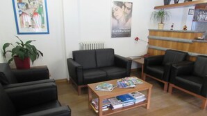 A modern living room with a black leather sofa, a wooden coffee table with magazines, a potted plant, and a poster on the wall. - Casa Alpina Don Guanella (Macugnaga)