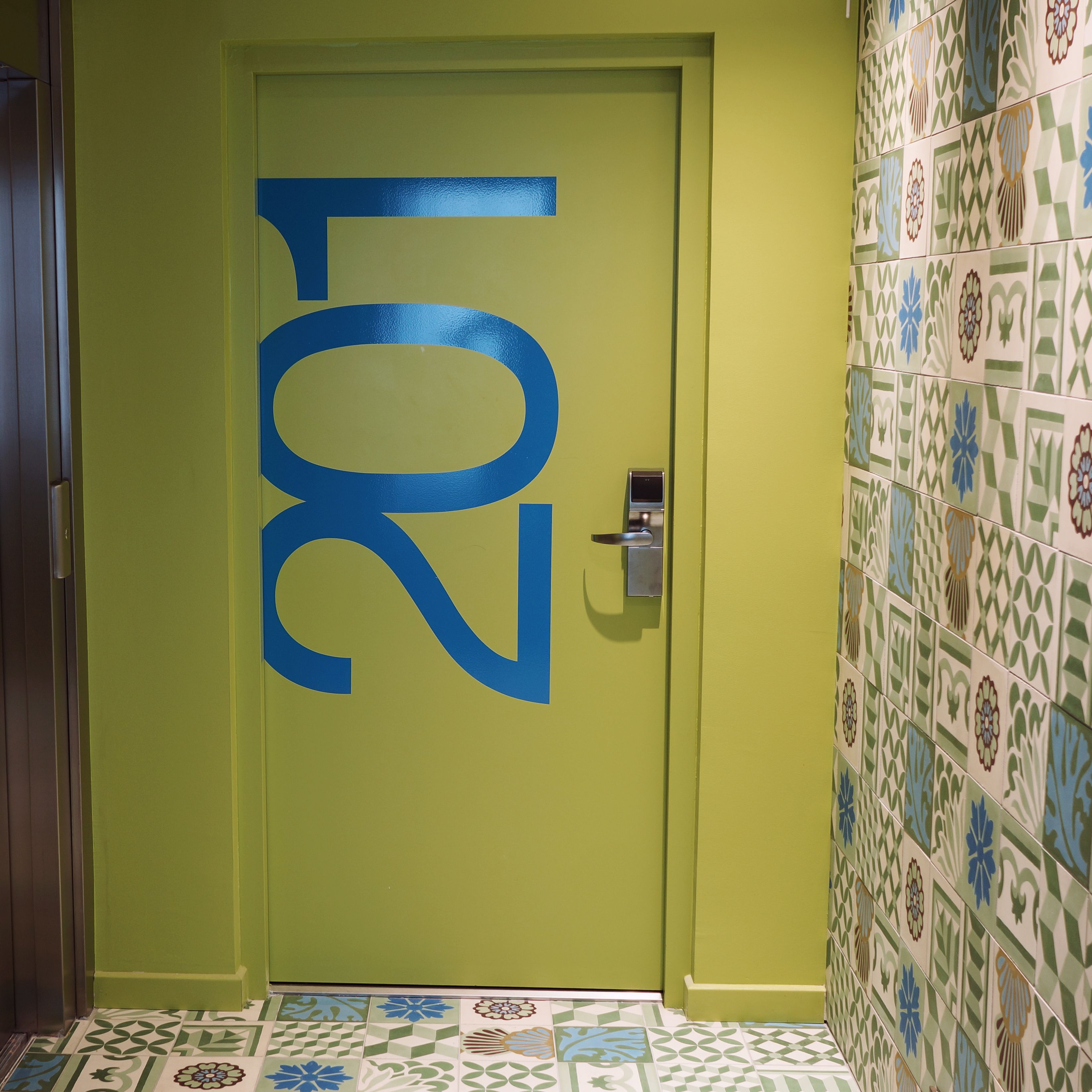 Una puerta con el número 201 pintado en azul, un candado con teclado numérico y una pared de azulejos con diseño geométrico.