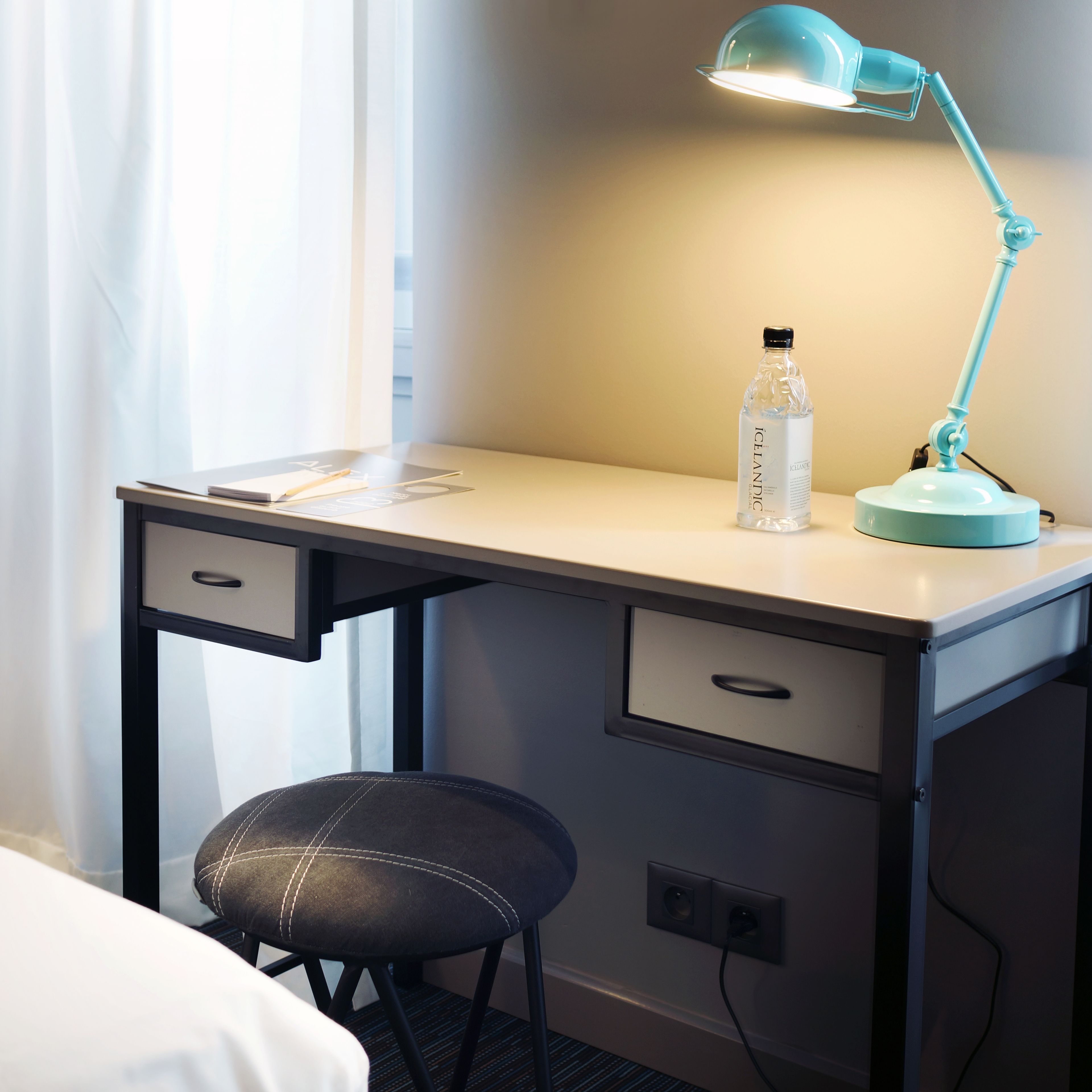 Habitación de hotel con escritorio, una silla, una lámpara y una botella de agua.