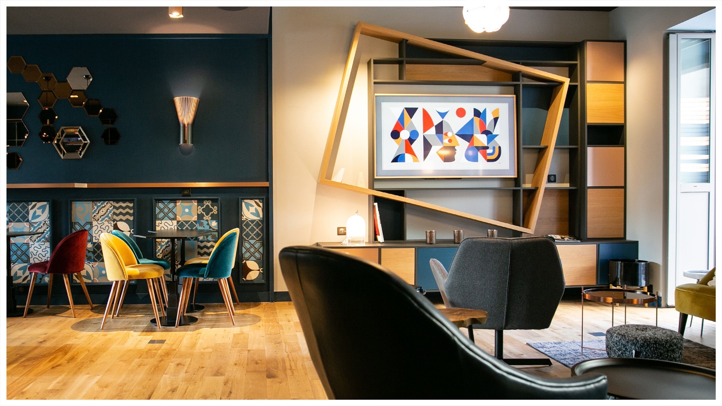 A modern interior with a wooden floor, colorful chairs, a black sofa, and a geometric art piece on the wall.