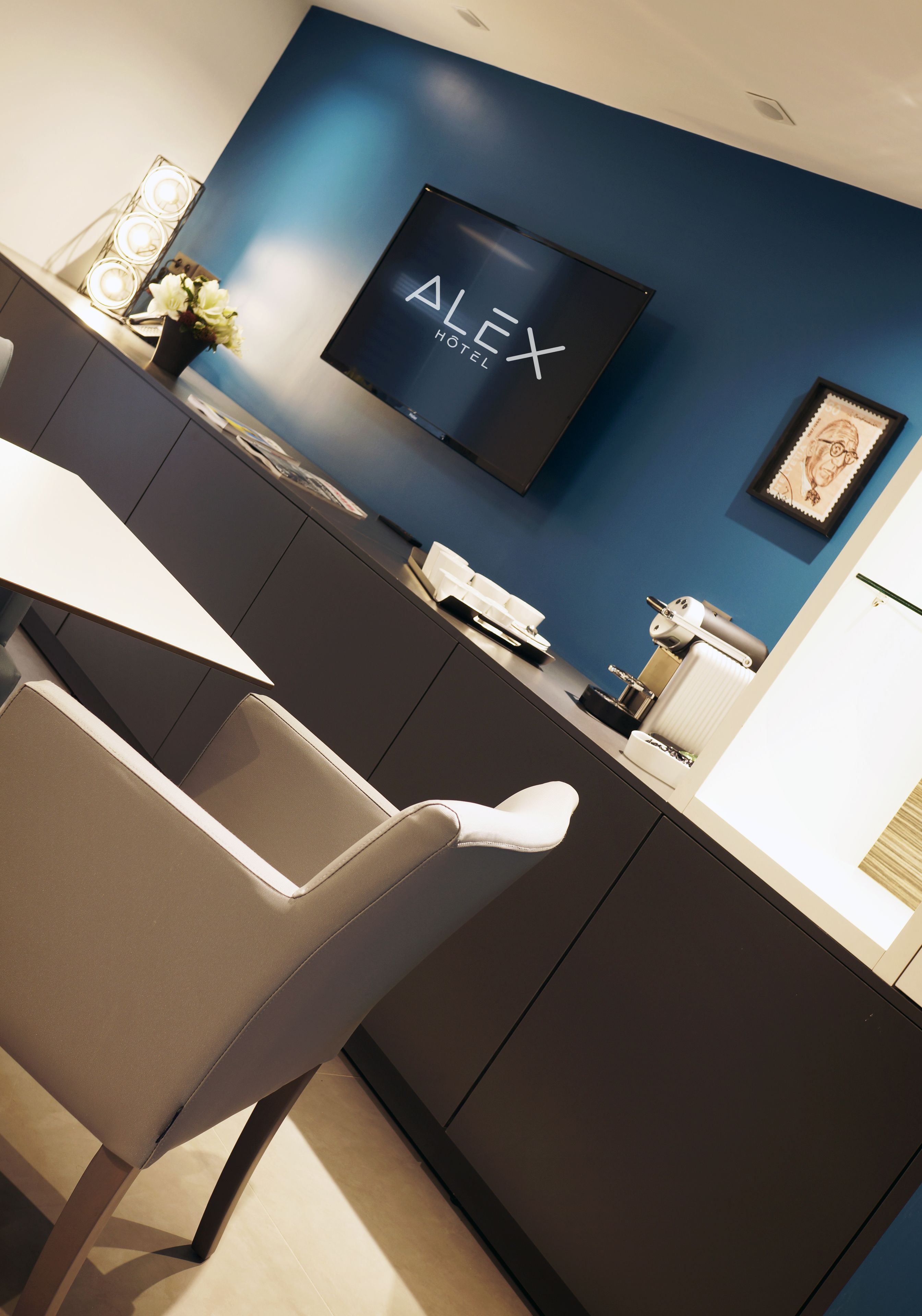 Une chambre d’hôtel moderne avec un mur d’accent bleu foncé, un téléviseur à écran plat fixé au-dessus d’un bureau en bois foncé et une chaise blanche.