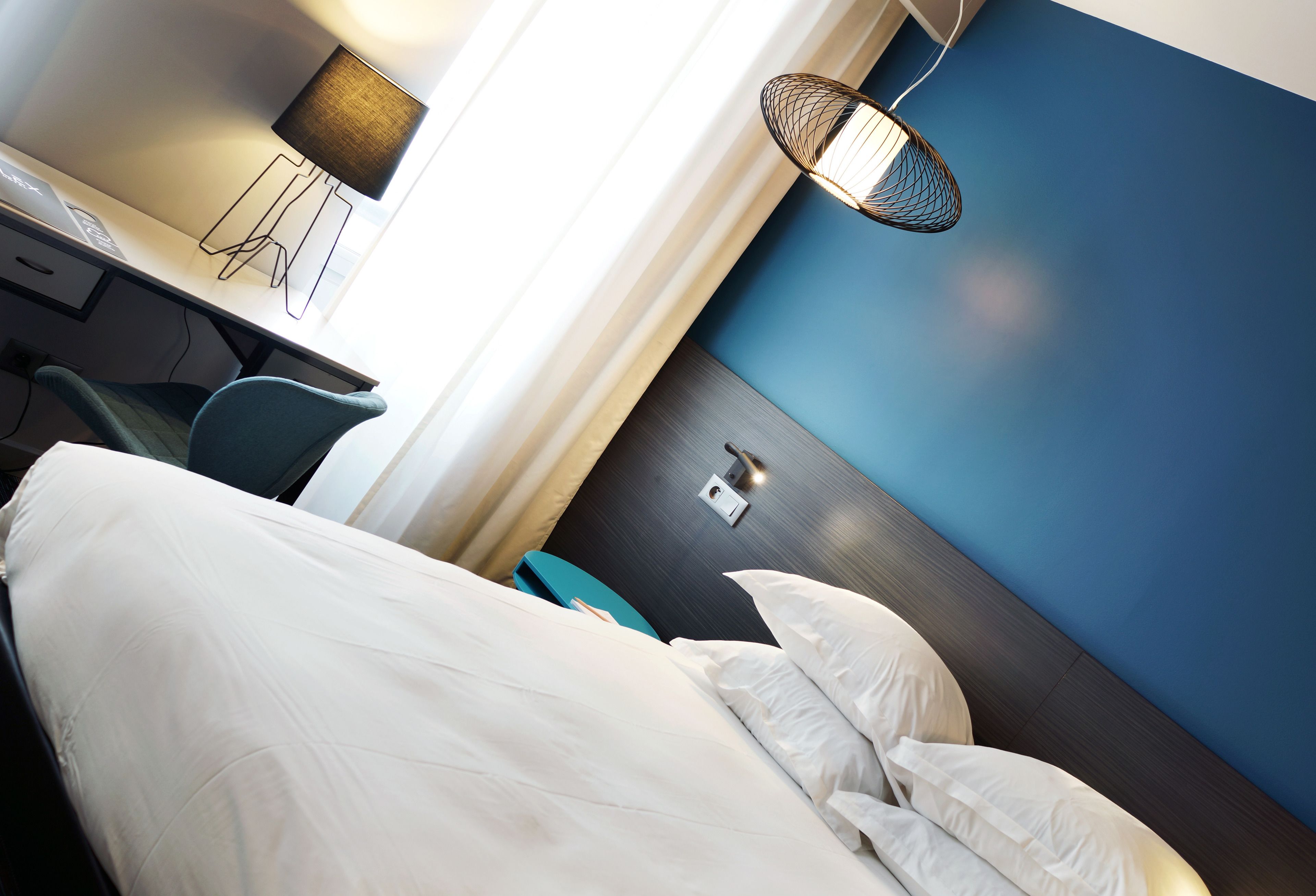 Una habitación de hotel con una cama, un escritorio con lámpara y una lámpara de pared.