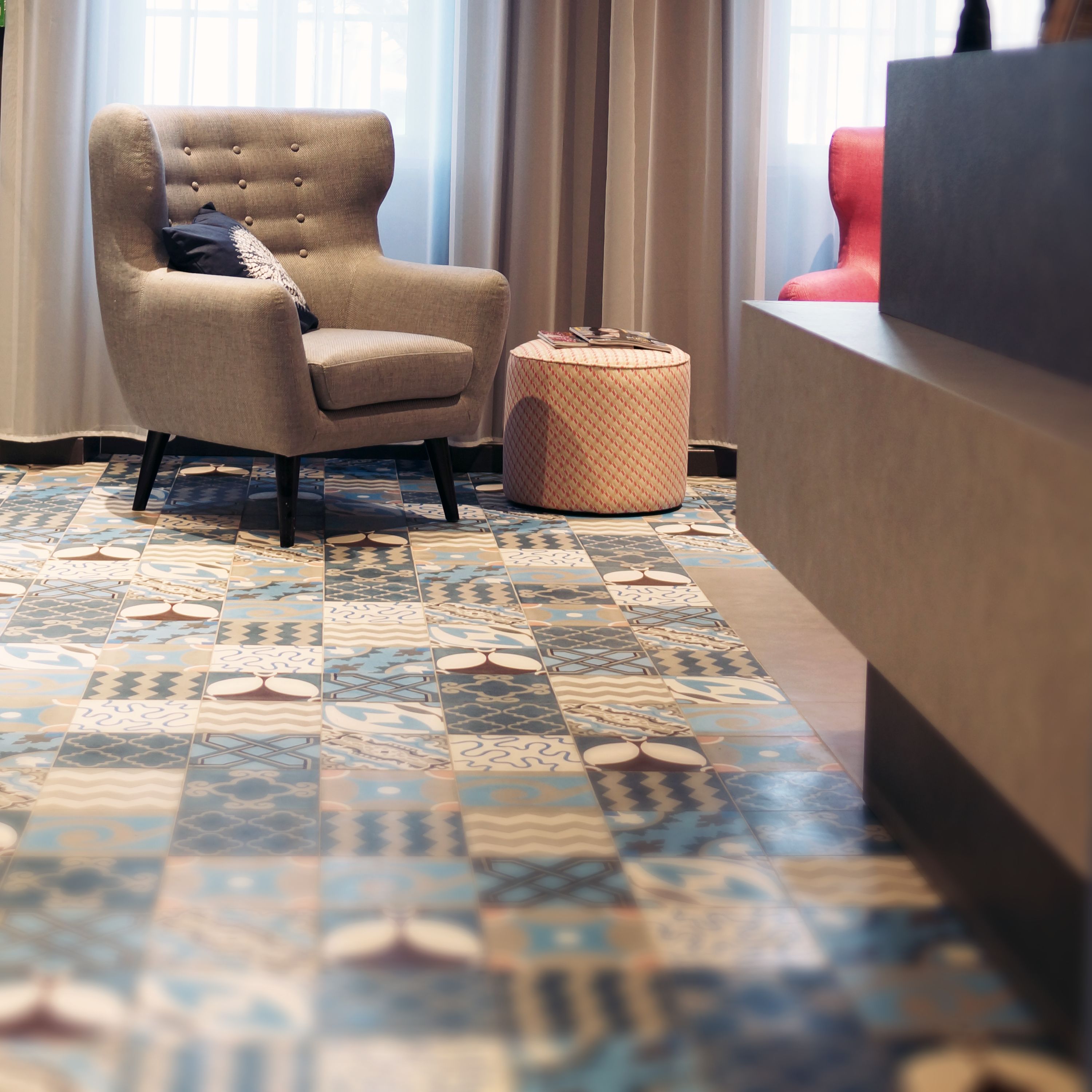 A room with a patterned floor, a tufted armchair, a round ottoman, and a reception desk.